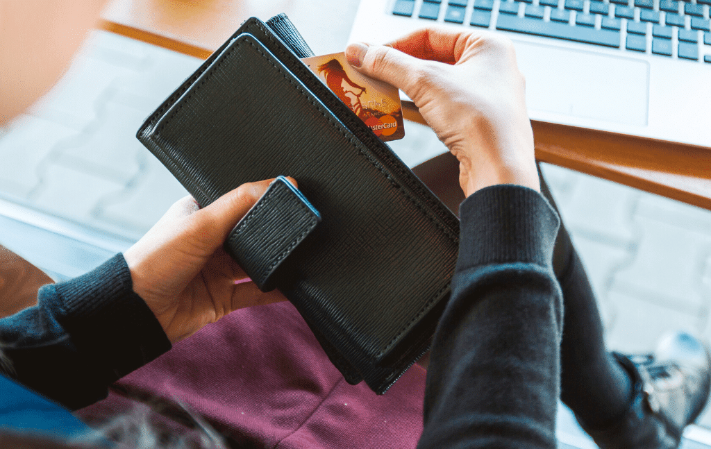 Person taking a payment card from a wallet beside a laptop
