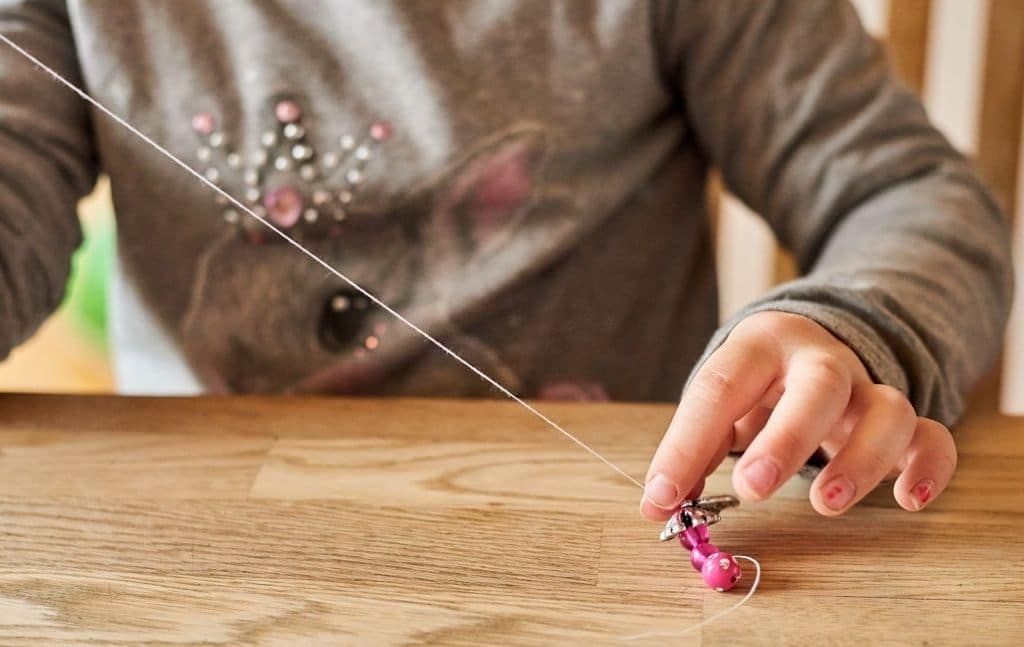 Child using a thin strand to make a bead craft