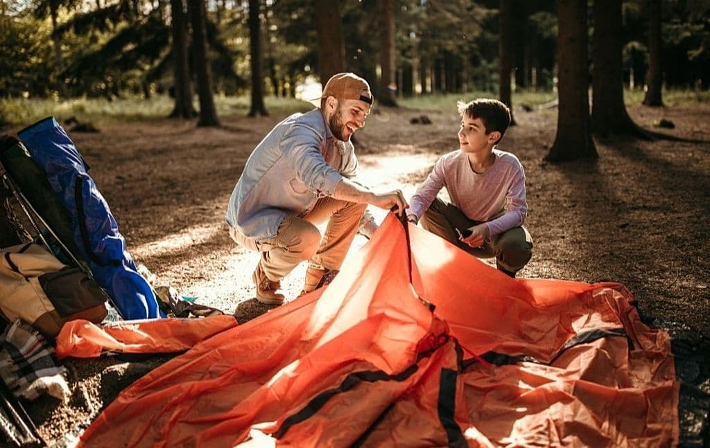 Adult and child setting up a tent at a campsite