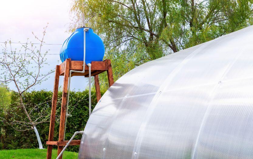 A large water storage barrel beside a greenhouse