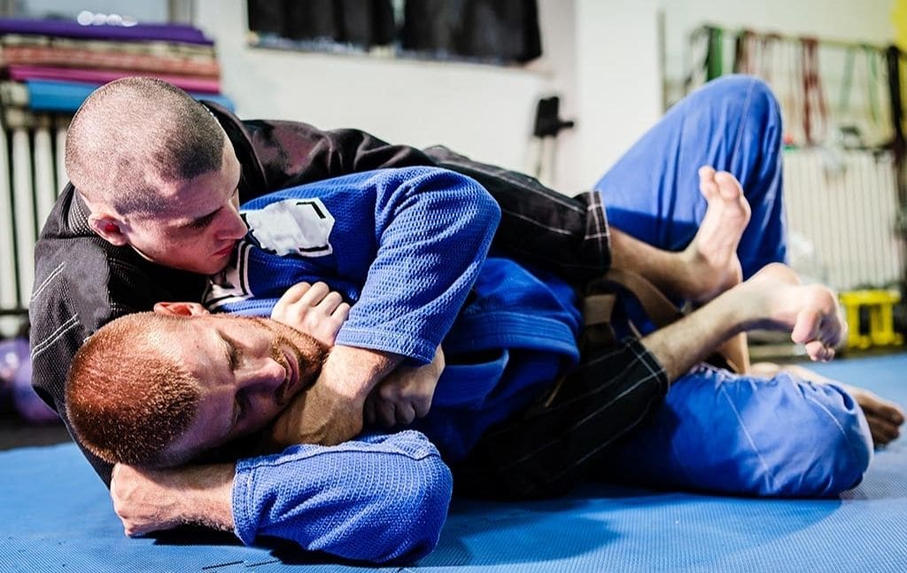 Two martial artists practicing a ground position on mats