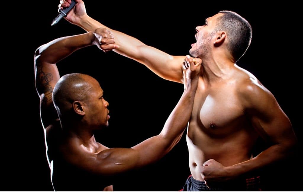 Two martial artists demonstrating a knife-defense scenario against a black background