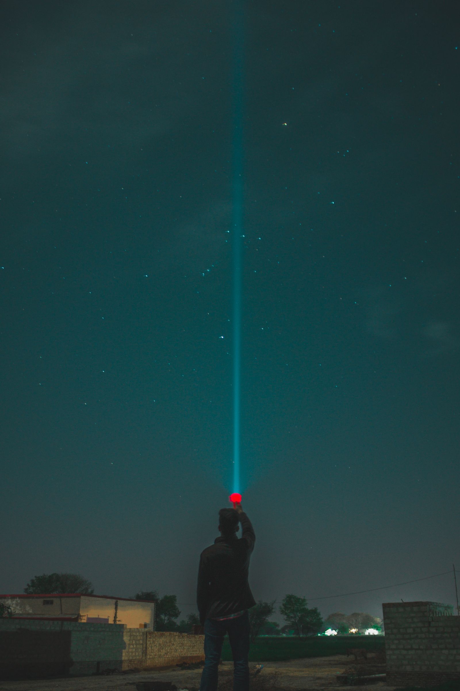 Person shining a flashlight beam into the night sky
