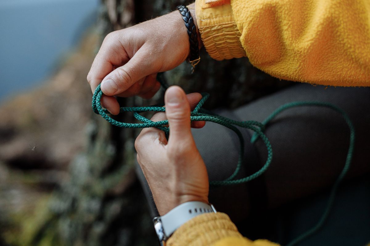 Hands tying a green rope knot outdoors