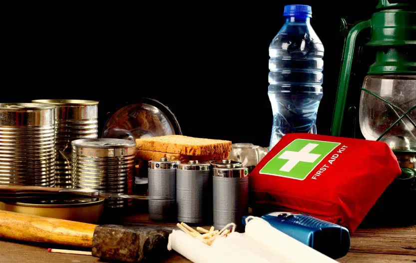 food cans, bread, water bottle, lamp and first aid kit on a wooden table