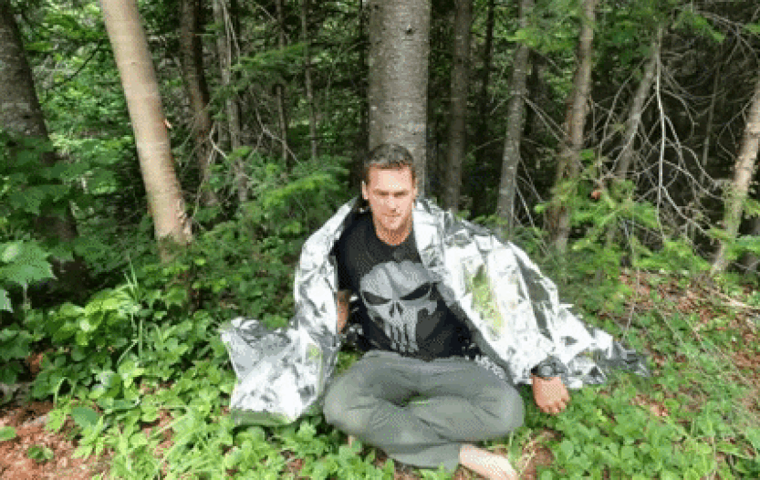 guy covering himself up with a mylar blanket in the woods
